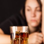 kobieta uzależniona od alkoholu, przed nią szklanka i butelka z alkoholem