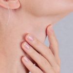 Kobieta trzyma się za szyję, za krtań. Odczuwa gulę w gardle.