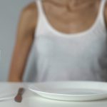 kobieta cierpiąca na anoreksję siedzi przed pustym talerzem i szklanką wody