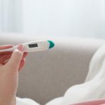 Kobieta patrzy na termometr, aby przekonać się, czy ma gorączkę po szczepieniu.