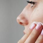 Kobieta przykłada płatek kosmetyczny do skóry, ma problem z kaszką na twarzy.