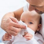 mężczyzna wyciera nos przeziębionemu niemowlakowi