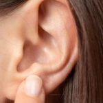 Kobieta przykłada palec do małżowiny usznej, ma problem z wysiękowym zapaleniem ucha