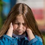 Dziewczynka trzyma się za uszy - doświadcza bólu ucha wywołanego zapaleniem ucha