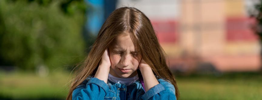 Dziewczynka trzyma się za uszy - doświadcza bólu ucha wywołanego zapaleniem ucha