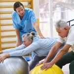 Dwie osoby wykonują ćwiczenia z kinezyterapii na piłkach pod nadzorem fizjoterapeuty