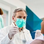Kobieta siedząca na fotelu dentystycznym - obok siedzi dentysta przygotowujący się do odbudowy zęba
