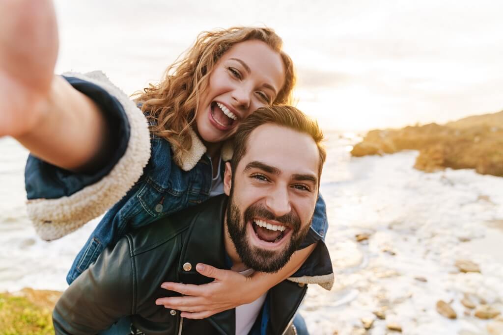 Image of beautiful young couple piggybacking while walking by seaside