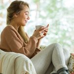 Kobieta siedzi w fotelu i pije rozgrzewającą herbatę na przeziębienie