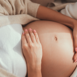 30. tydzień ciąży - kobieta w 30. tygodniu ciąży leży na łóżku i trzyma się za brzuch