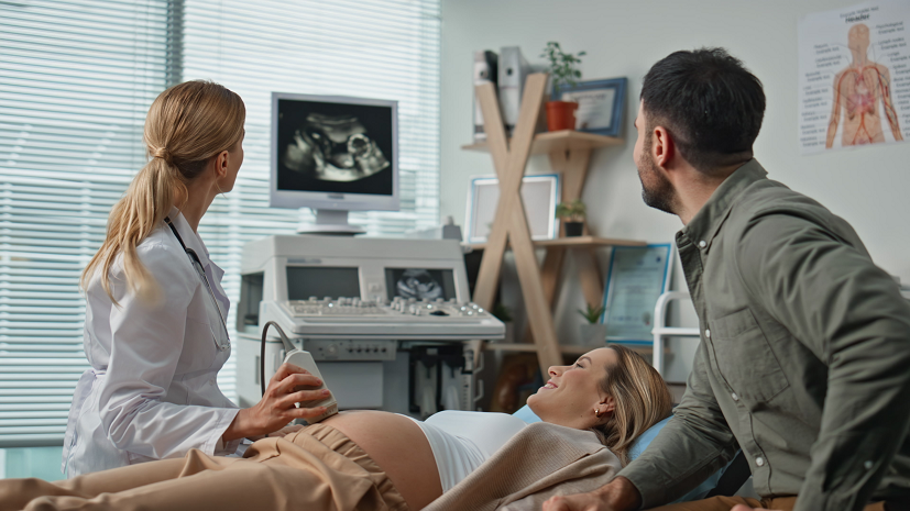 Lekarka wykonuje USG kobiecie w 31. tygodniu ciąży. Obok siedzi uśmiechnięty mężczyzna