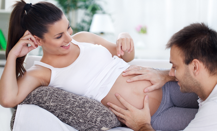 Kobieta w 33. tygodniu ciąży leży na kanapie - razem z mężem wyczuwają ruchy dziecka w brzuchu