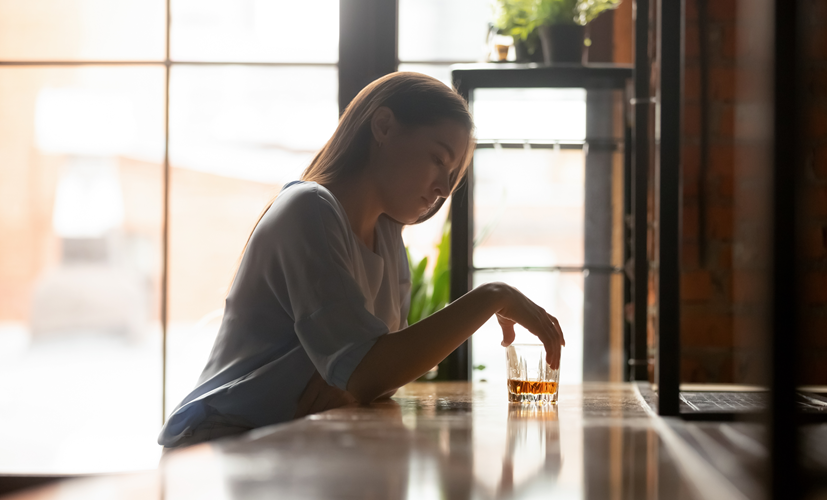 Kobieta patrzy na szklankę z alkoholem - zaburzenia psychiczne mogą występować po alkoholu